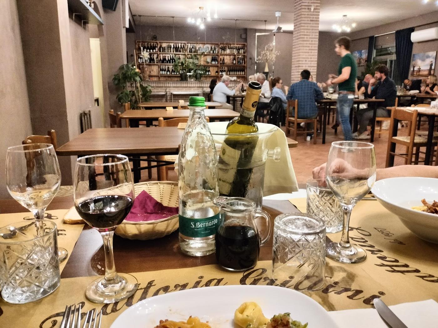 La sala della trattoria, con i mattoni a vista e la parete delle bottiglie di vino