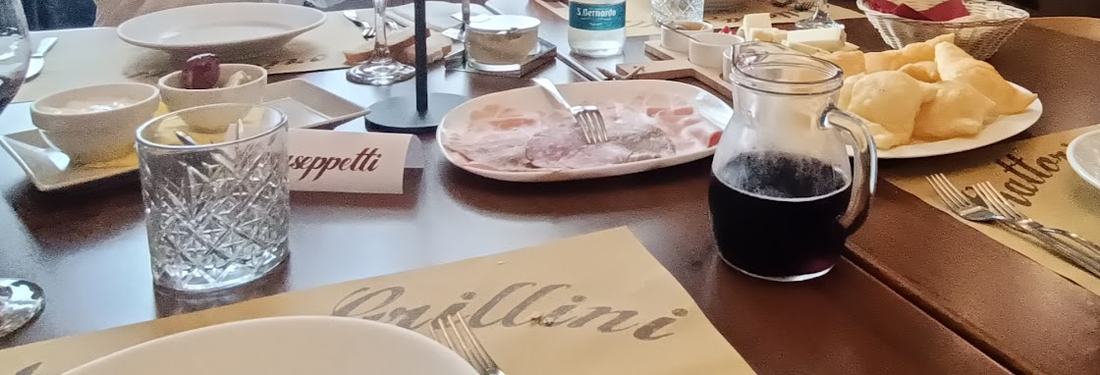 Tavola apparecchiata con salumi, gnocco fritto e un bicchiere di rosso sulle tovagliette Grillini